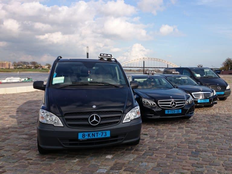 Vier taxi's van Taxi Centrale Nijmegen op de Waalkade in Nijmegen, met de Waalbrug op de achtergrond